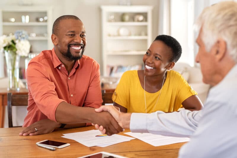 advisor shaking hands with smiling man across table while woman watches