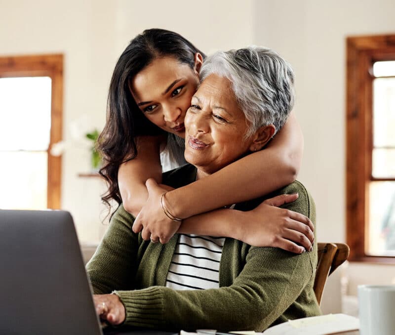 younger woman hugging older woman on laptop