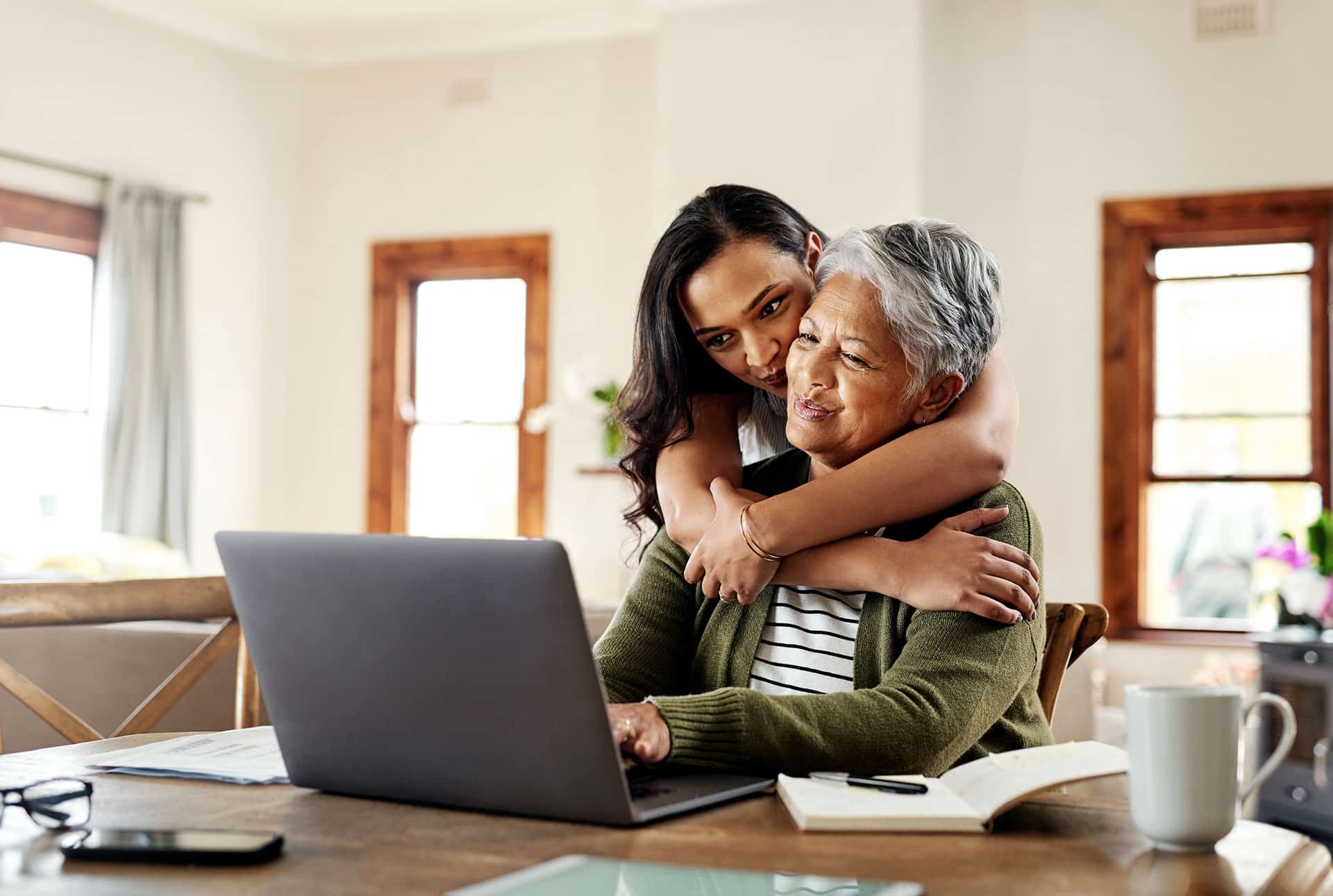 younger woman hugging older woman on laptop