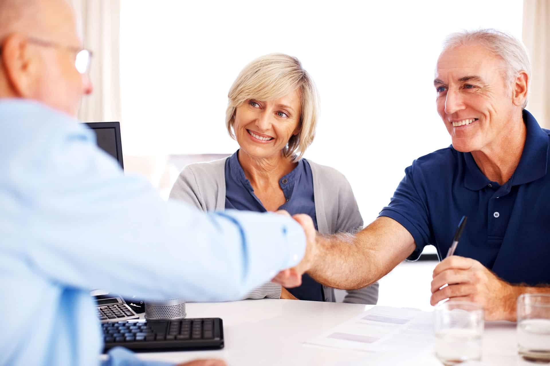 advisor shaking man's hand across table, woman smiling